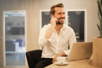 Man smiling, talking on the phone and drinking coffee